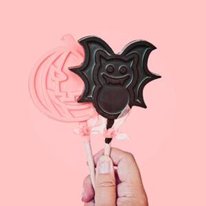 Chocolate lollipops in shape of pumpkin and bat. Pink pastel Halloween concept greeting card